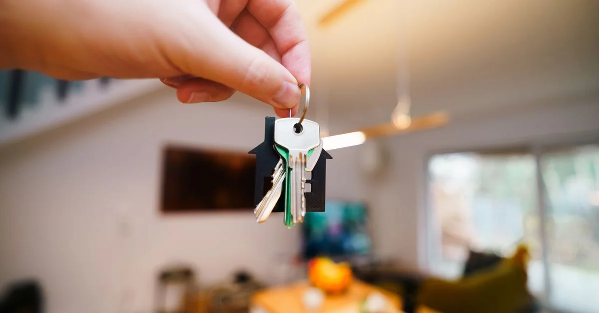 Una mano sostiene las llaves con un llavero de casa dentro de un espacio habitable moderno y bien iluminado.