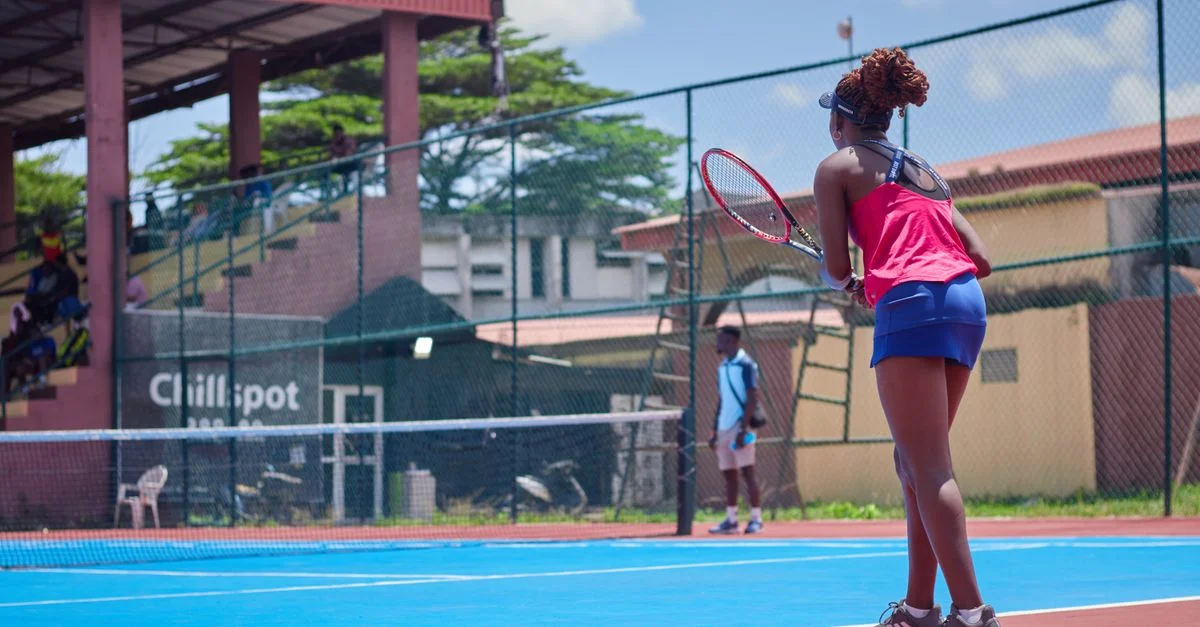 Una mujer jugando tenis en un día soleado, mostrando sus habilidades en una cancha al aire libre.