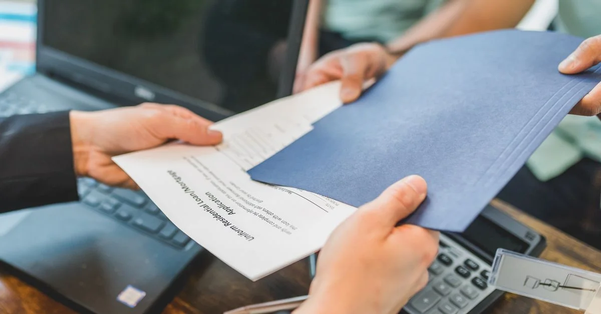 Primer plano de manos intercambiando documentos inmobiliarios en un entorno de oficina.