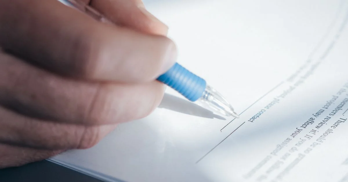 Una imagen en primer plano que muestra una mano sosteniendo un bolígrafo mientras firma un documento.