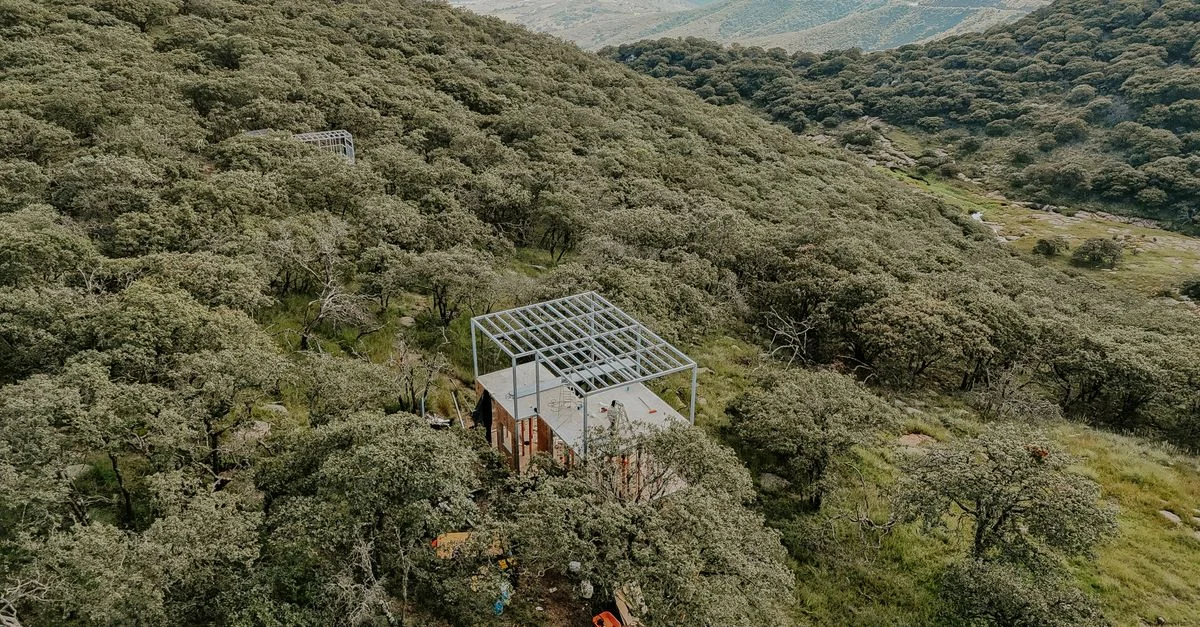 Vista aérea de un sitio de construcción en un bosque denso en la ladera de una montaña, que muestra el progreso industrial y la naturaleza.