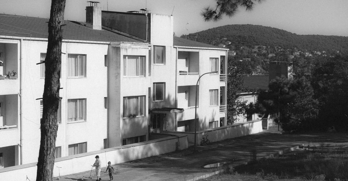 Niños juegan cerca de un edificio residencial urbano rodeado de naturaleza en monocromo