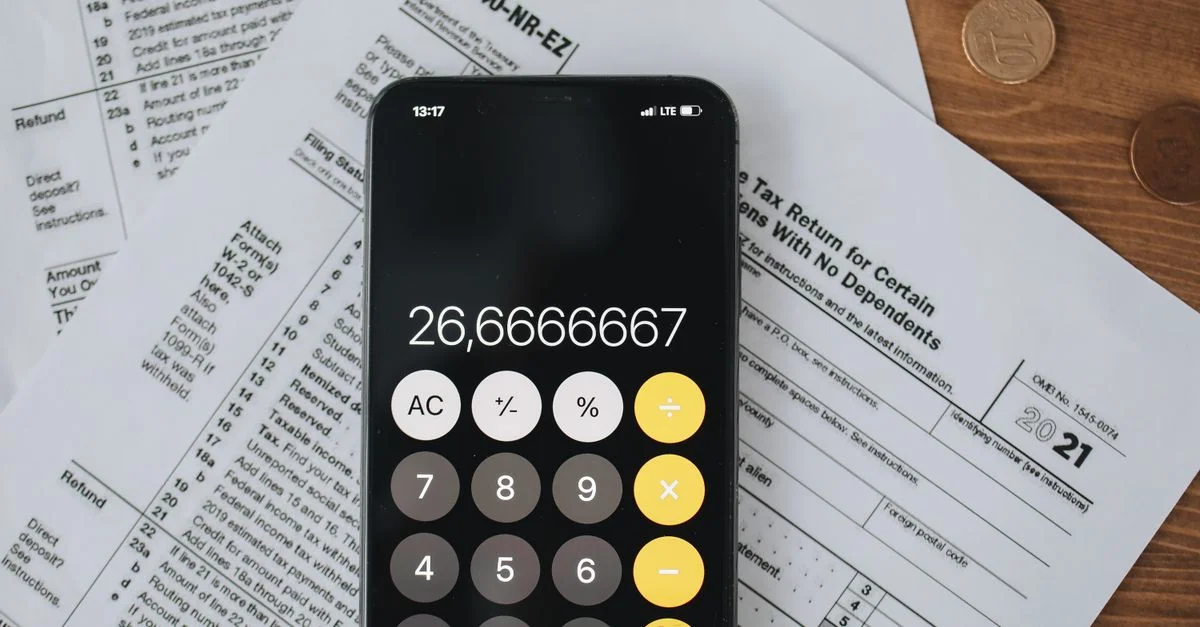 Calculadora de smartphone sobre formularios de impuestos con monedas, simbolizando el cálculo de impuestos y finanzas.