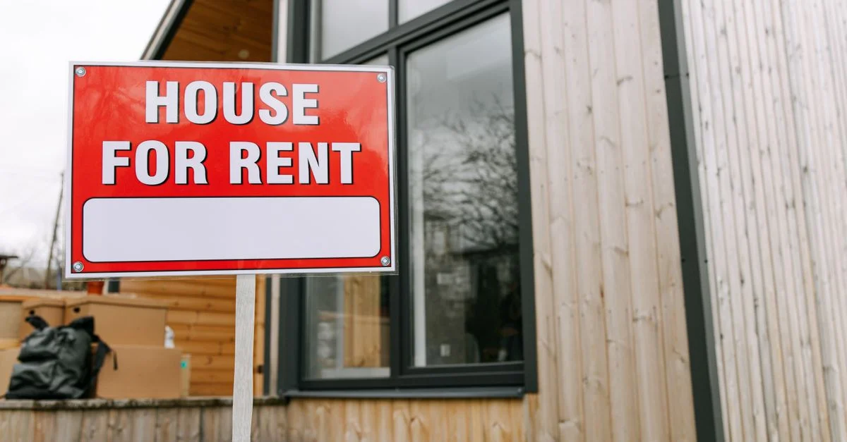 Cartel rojo 'Casa en Alquiler' frente a una casa moderna de madera.