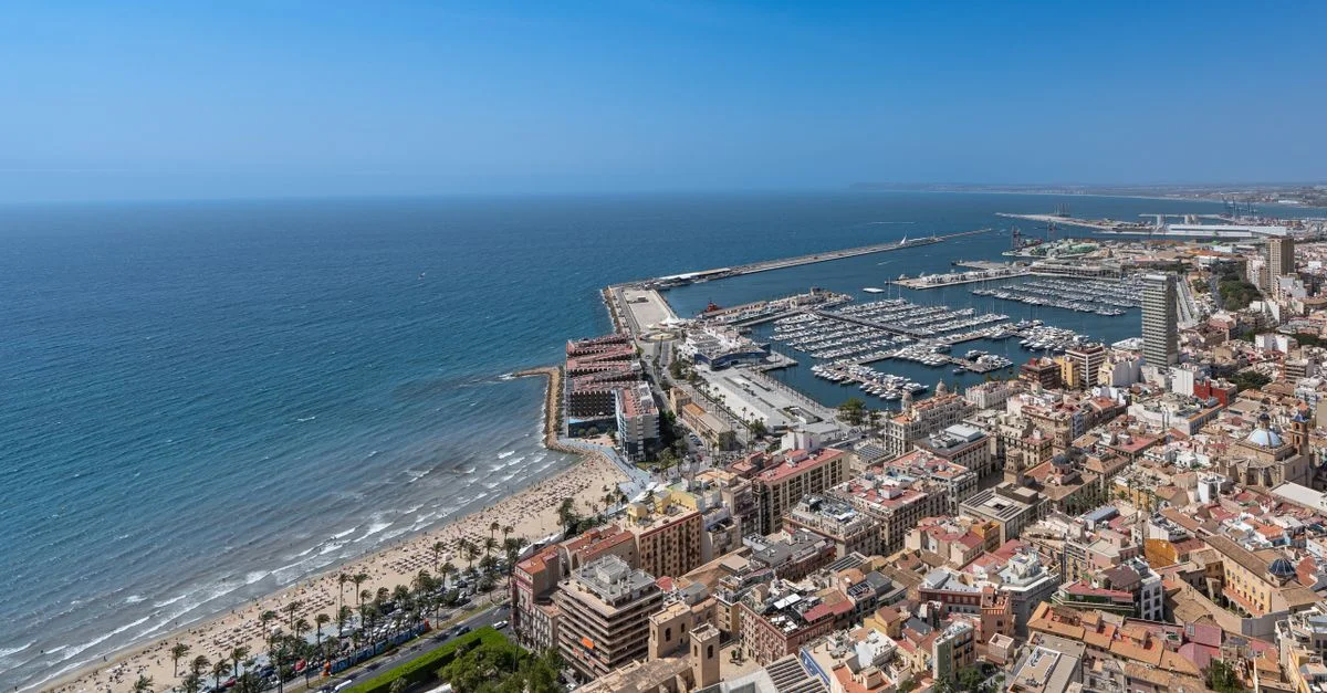 Vista aérea vibrante de la costa de Alicante, de la marina y del paisaje urbano bajo un cielo azul claro.